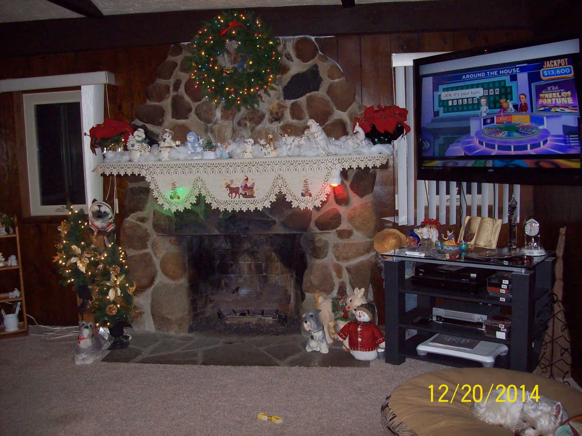 Cozy living room with a stone fireplace, holiday decorations, a Christmas tree, and a TV.