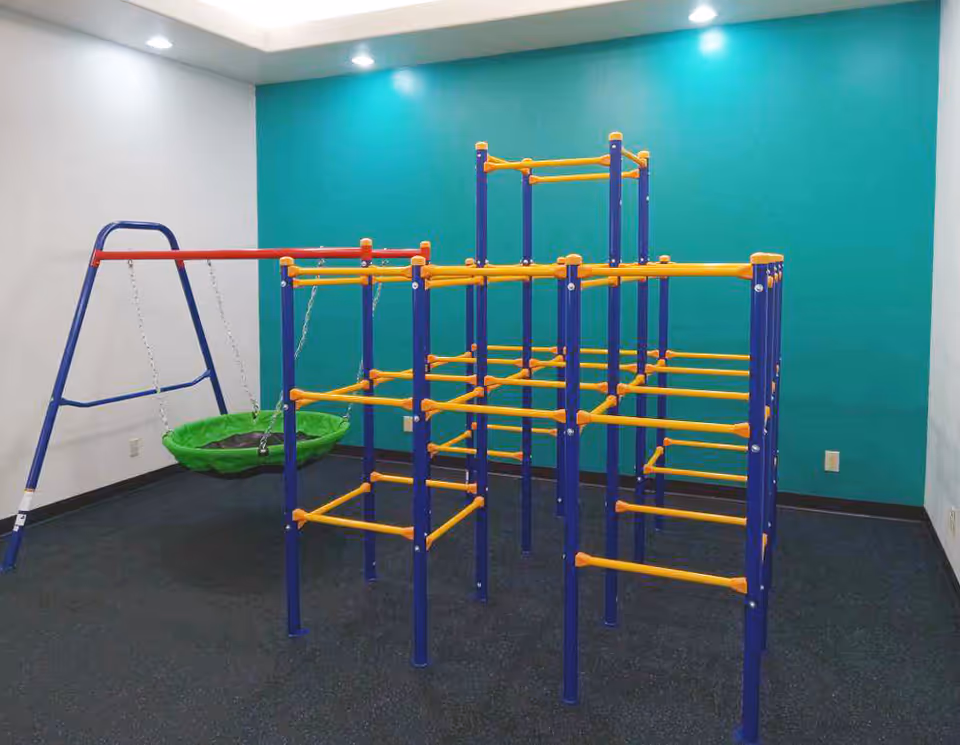 Indoor play gym with blue and yellow climbing structure and green swing in a teal room