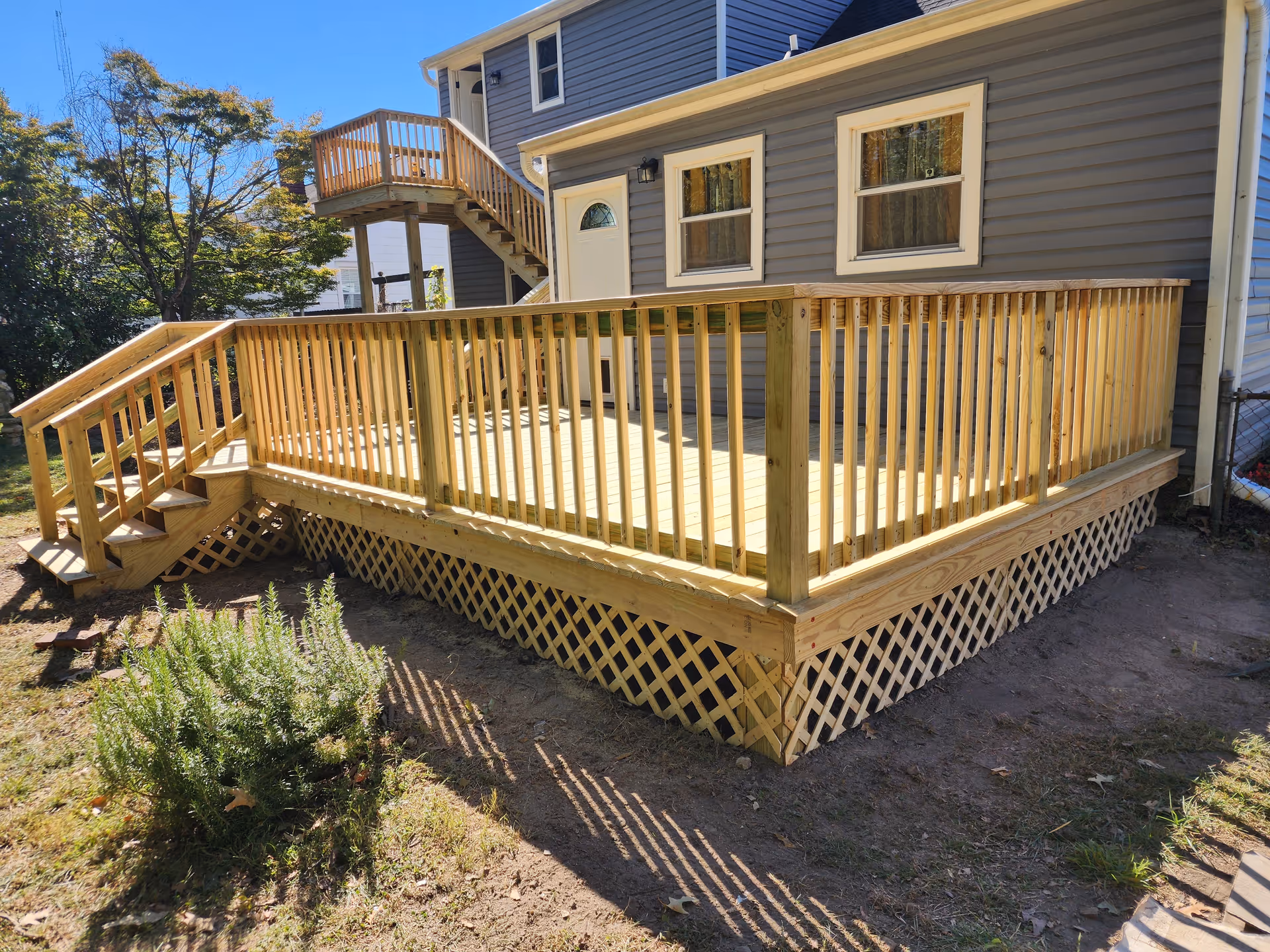 Backyard wooden deck attached to a gray house with stairs and railing.