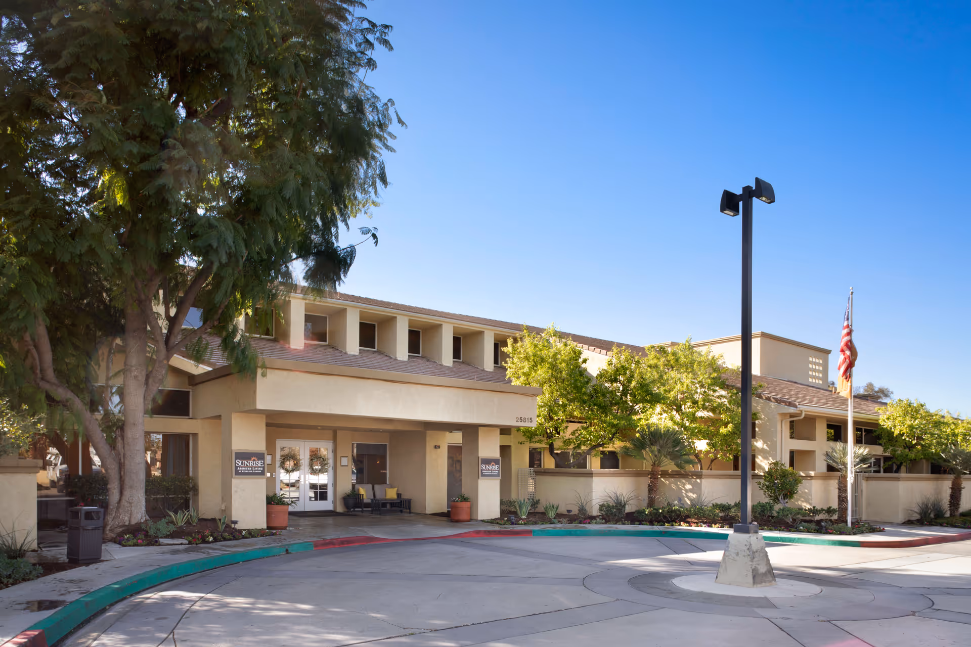 Exterior of Sunrise at Sterling Canyon with entrance, trees, flagpole, and blue sky.