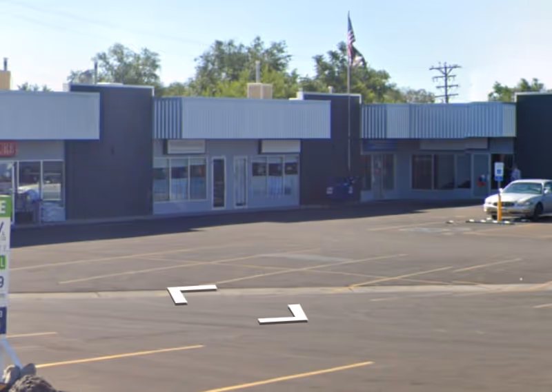 A single-story building with several storefronts and a mostly empty parking lot.