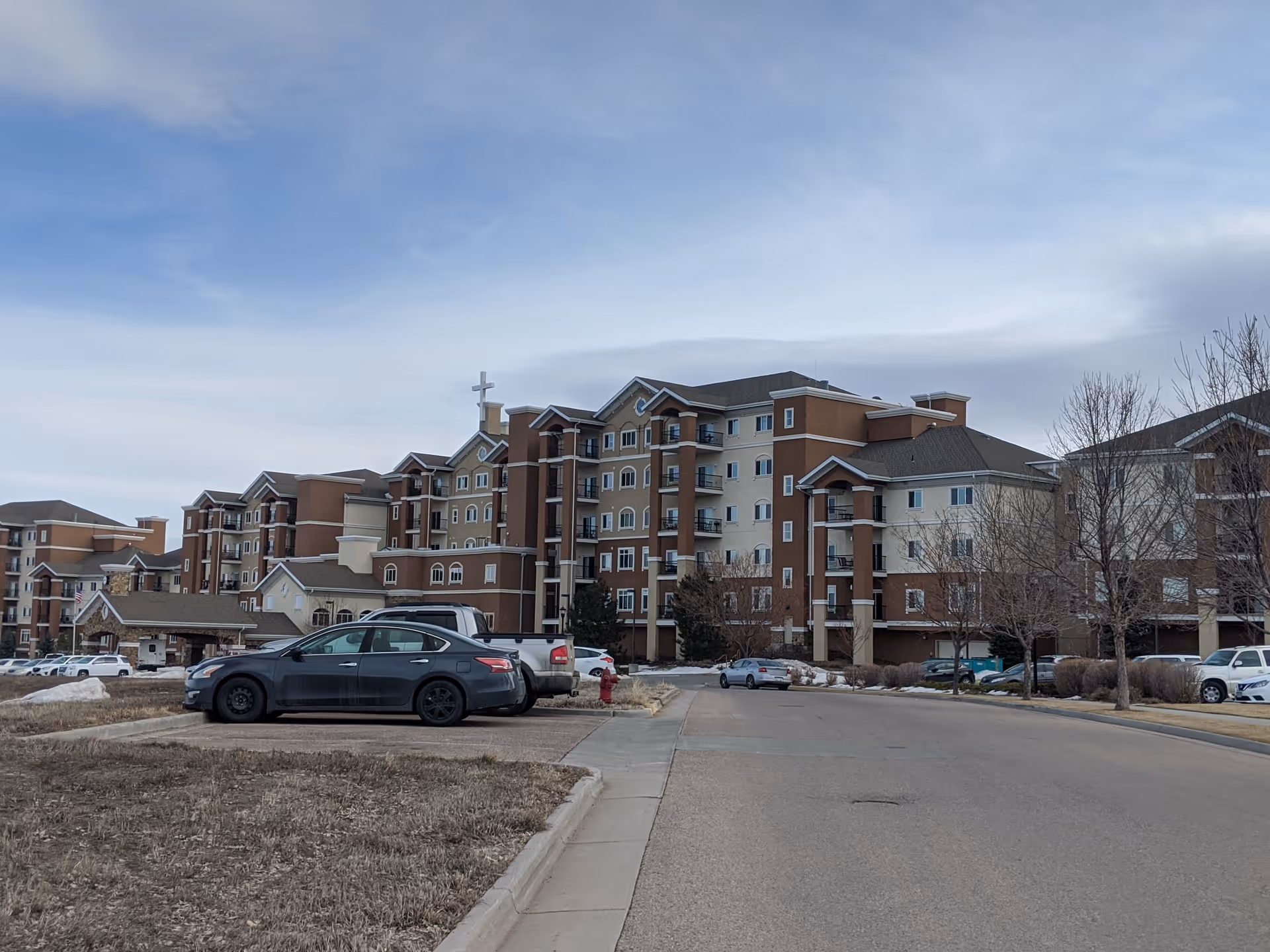 Exterior view of a large multi-story senior living facility with parked cars.