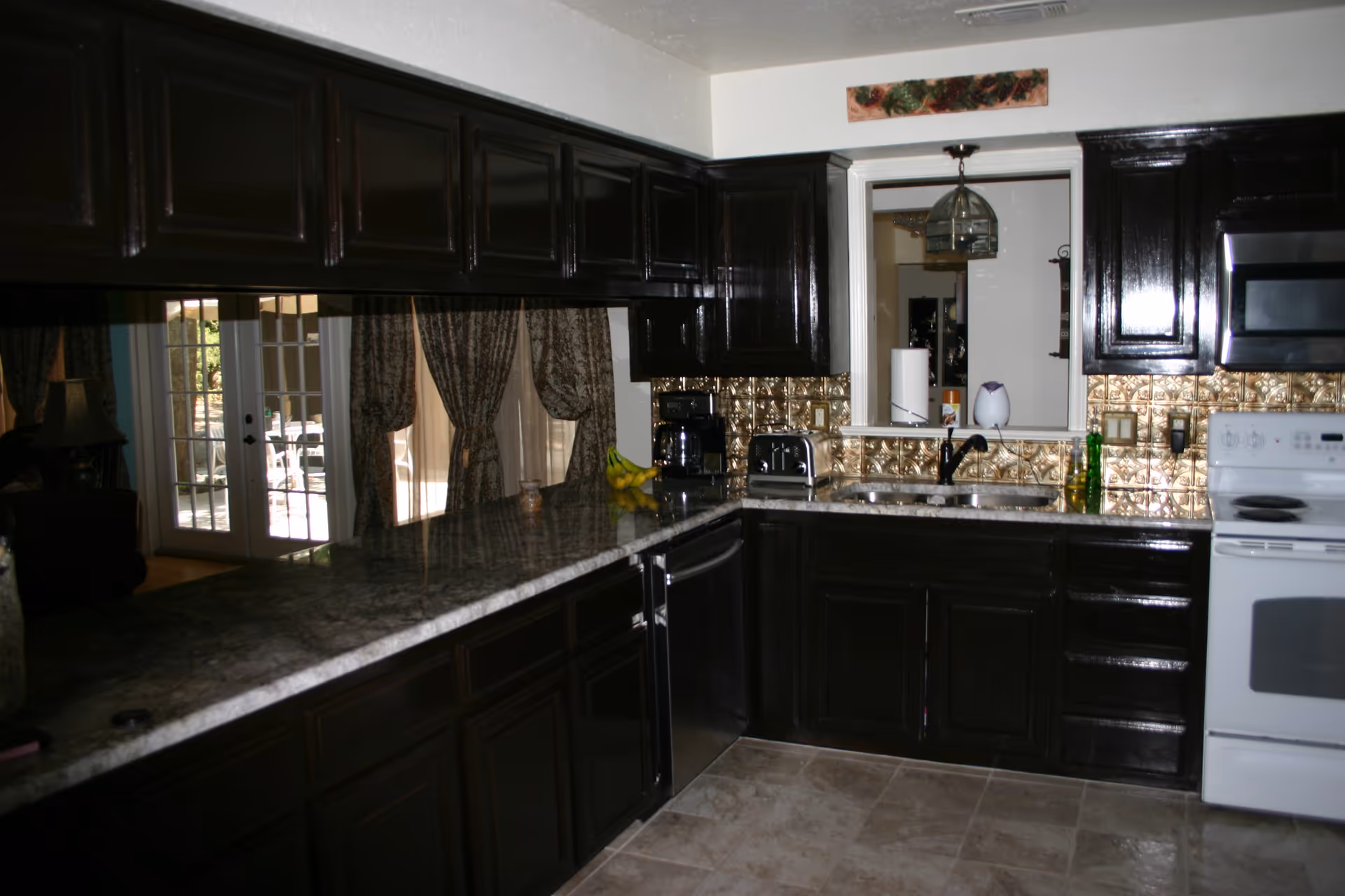 Dark wood kitchen with granite countertops and stainless appliances, curtains at the doorway.