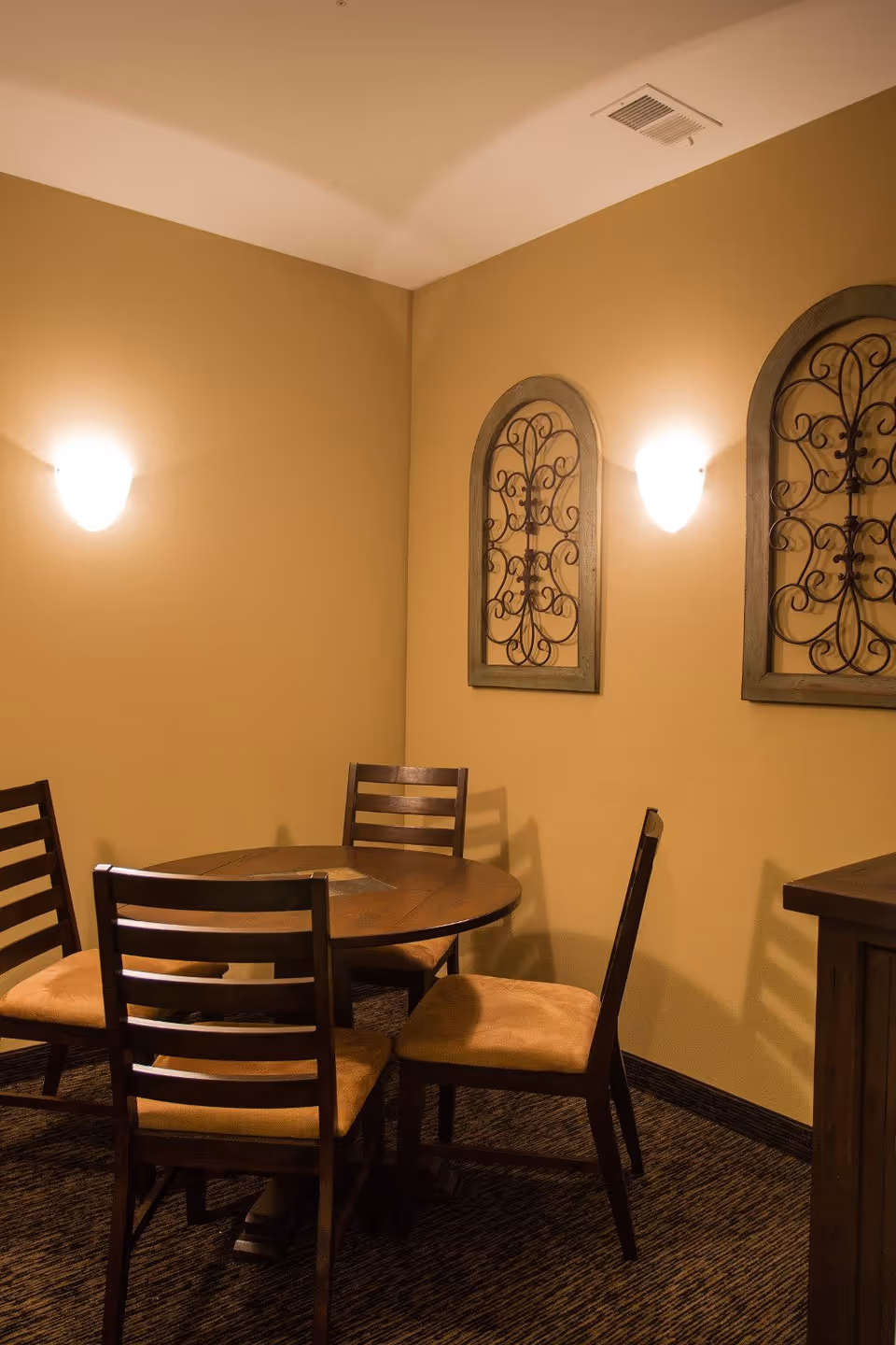 Round wooden dining table with chairs in a warmly lit beige dining area.