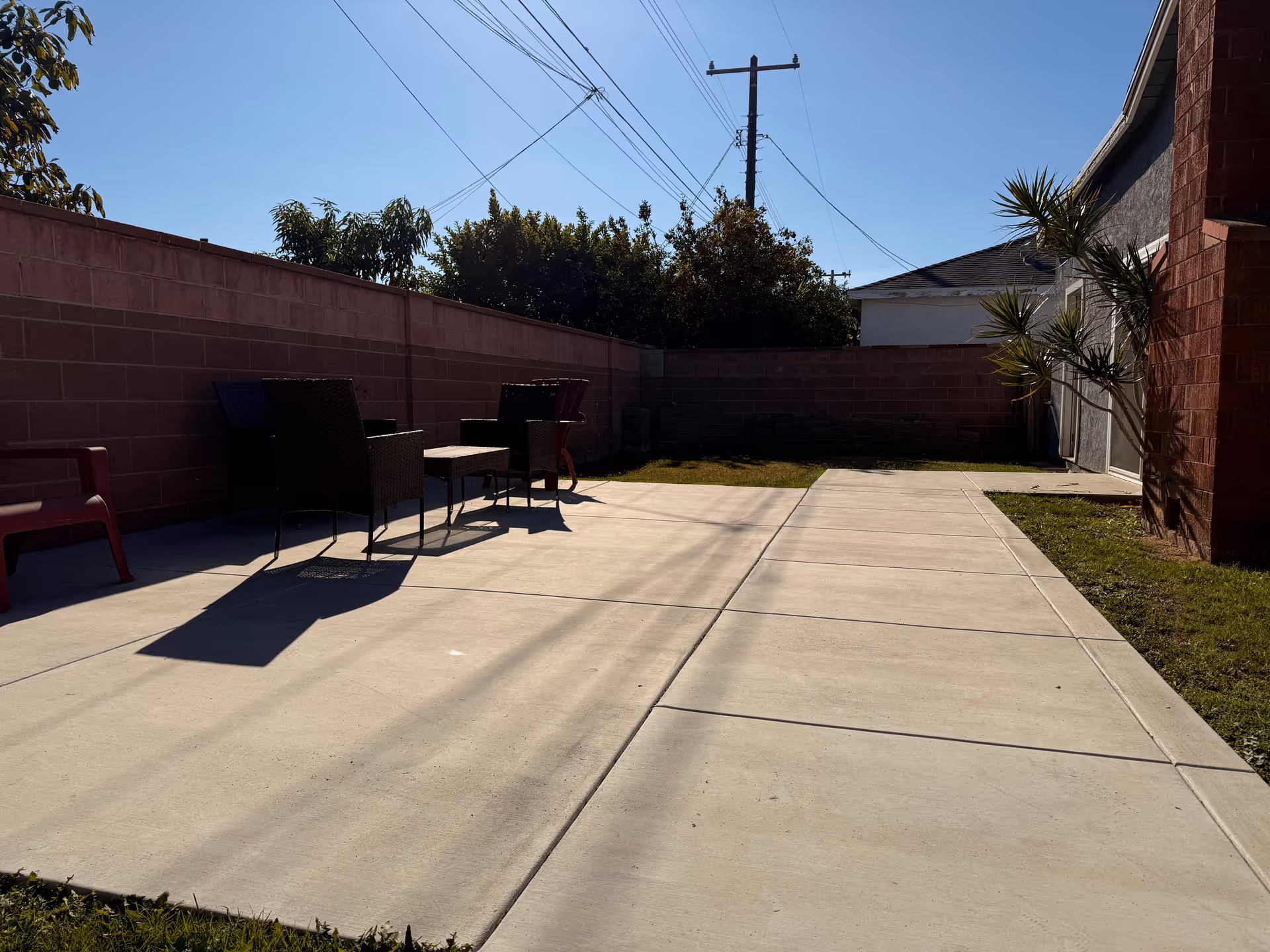 Sunny outdoor patio with chairs and tables beside a brick wall.