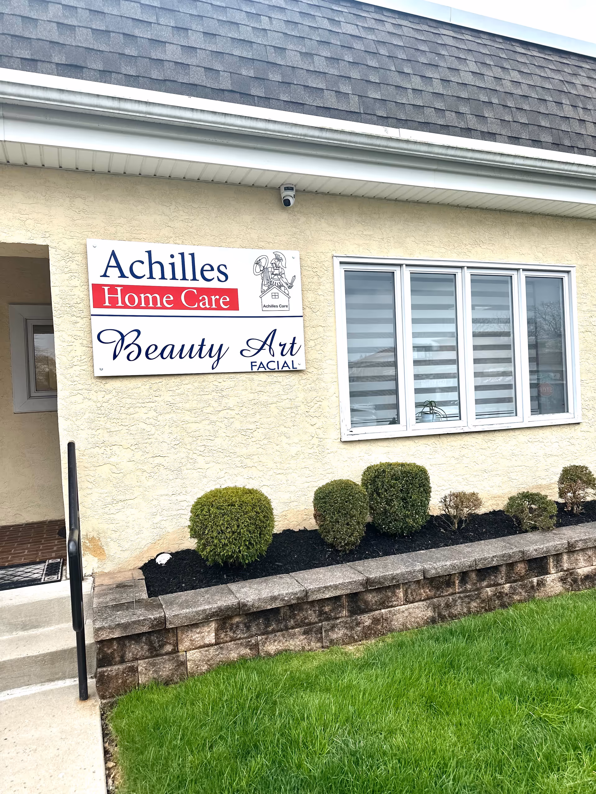 Front exterior of a beige building with an Achilles Home Care sign and a window.