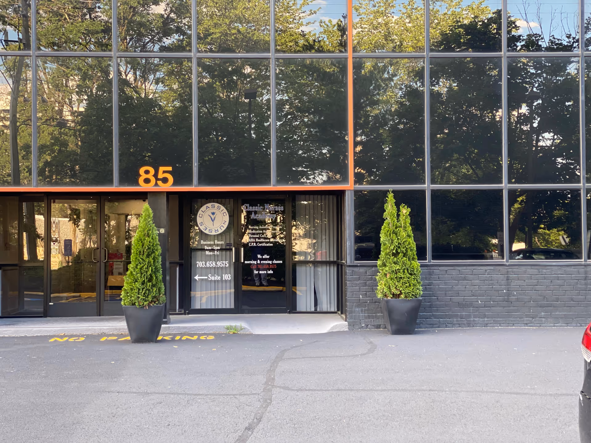 Glass-front building entrance with two potted evergreens and the number 85.