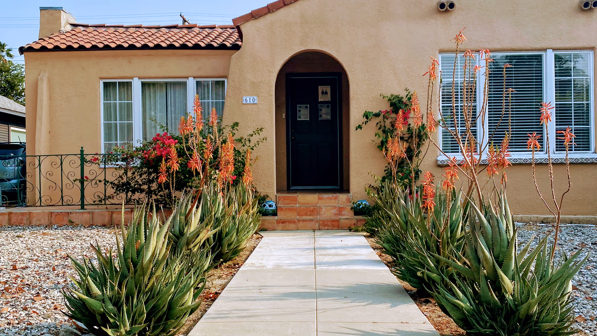 Front entrance of a tan stucco senior living building with an arched doorway and desert plants.