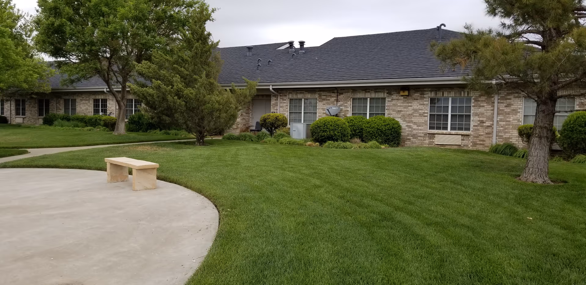 Exterior view of The Seasons Assisted Living facility with green lawn, trees, and a bench.