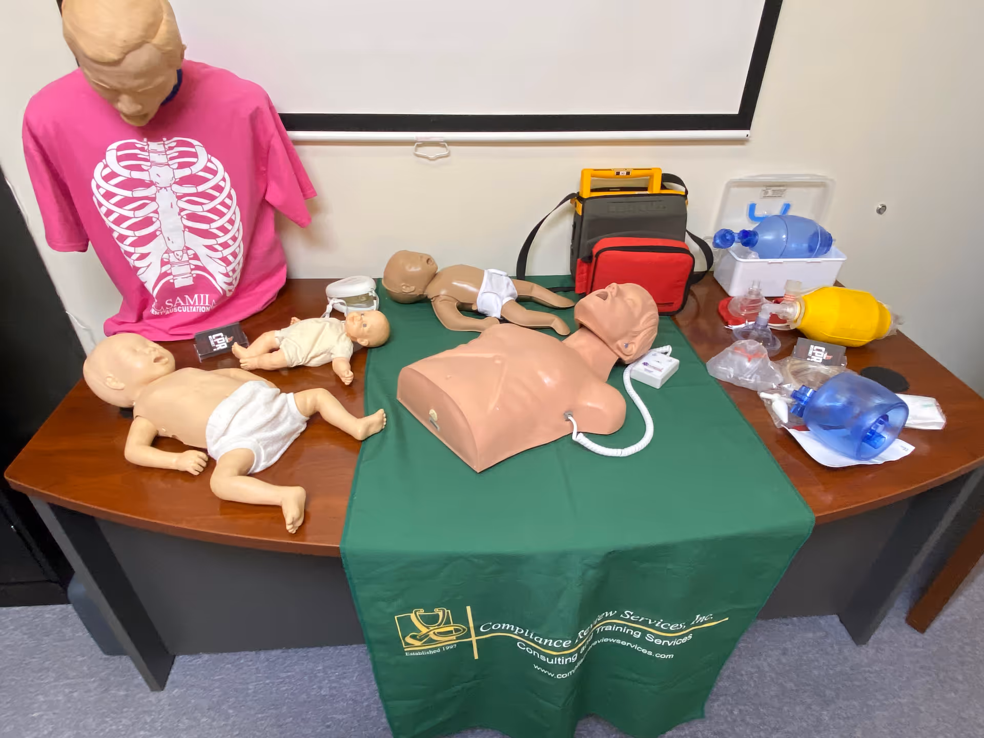 CPR mannequins and medical training gear arranged on a table in a classroom setting.