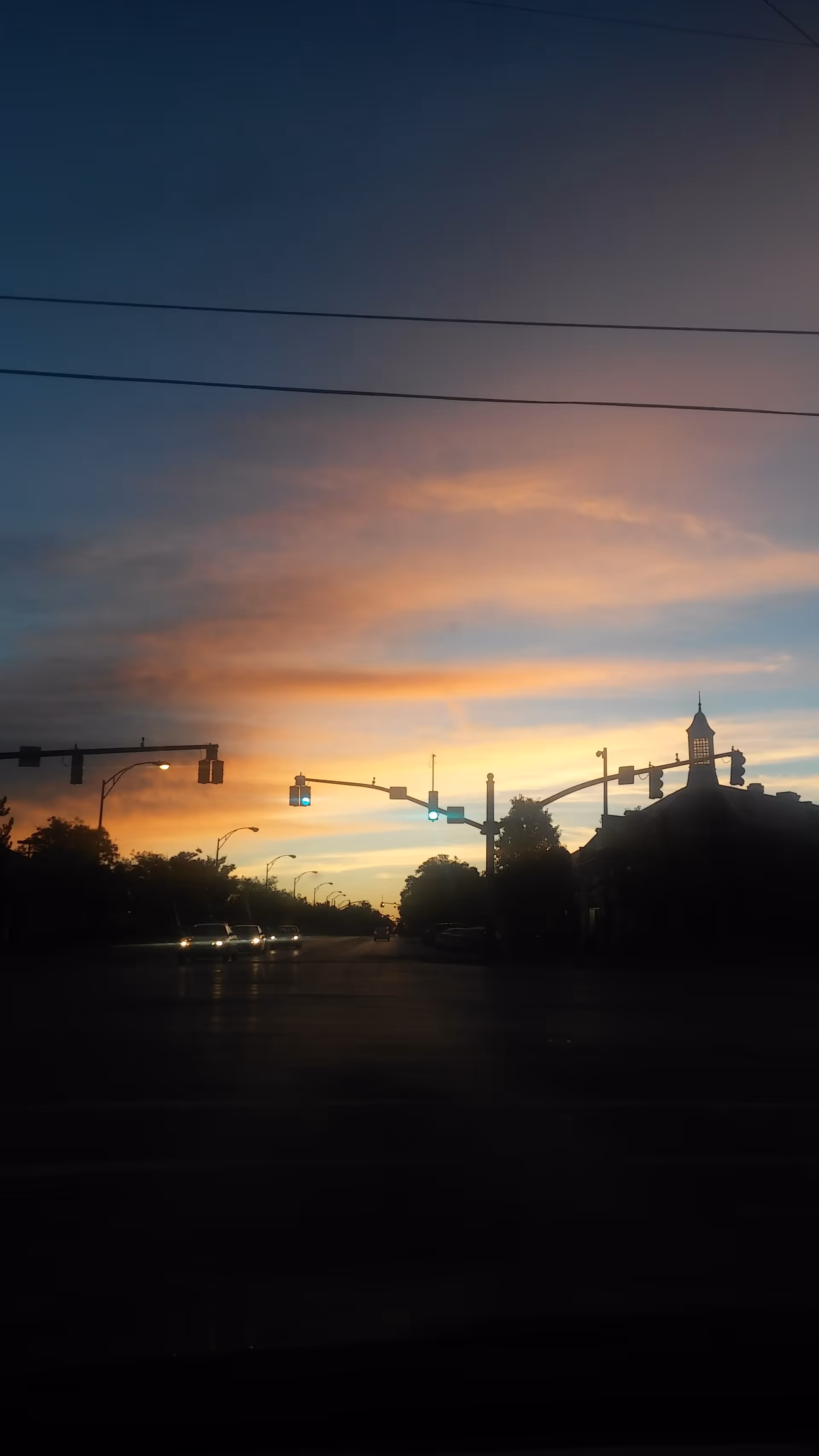 Sunset sky over a street with traffic lights and silhouetted buildings.
