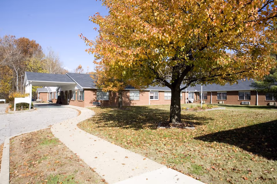 Brick senior care building with curved walkway and autumn tree in front yard.
