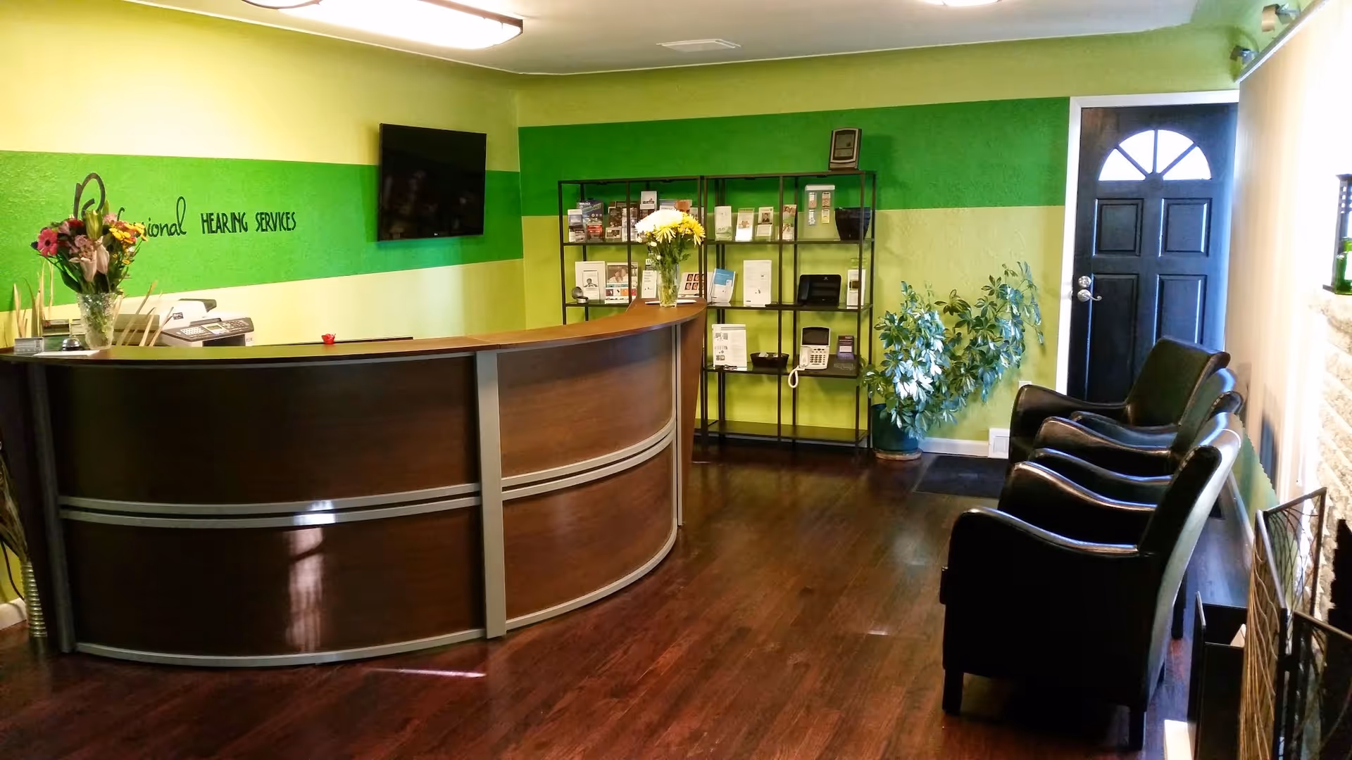Reception desk with curved wood counter, green walls, chairs, and brochure shelves in lobby.