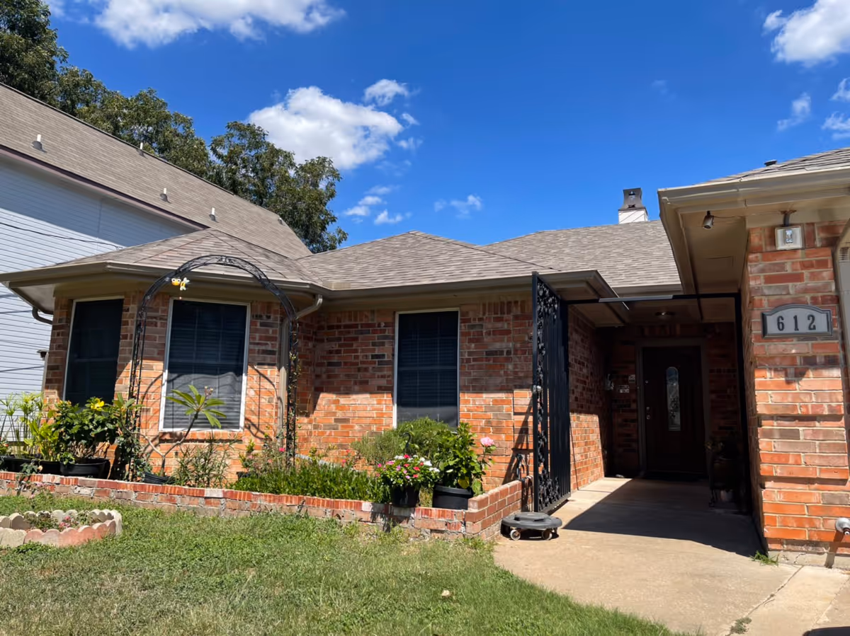 Brick senior living facility exterior with garden beds, a metal entry gate, and blue sky.