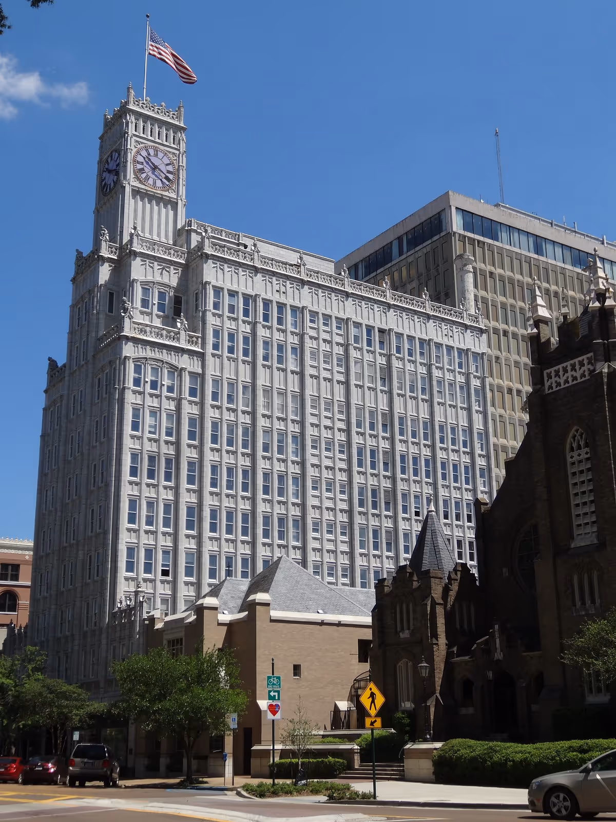 Tall historic building with clock tower and American flag on a city street.