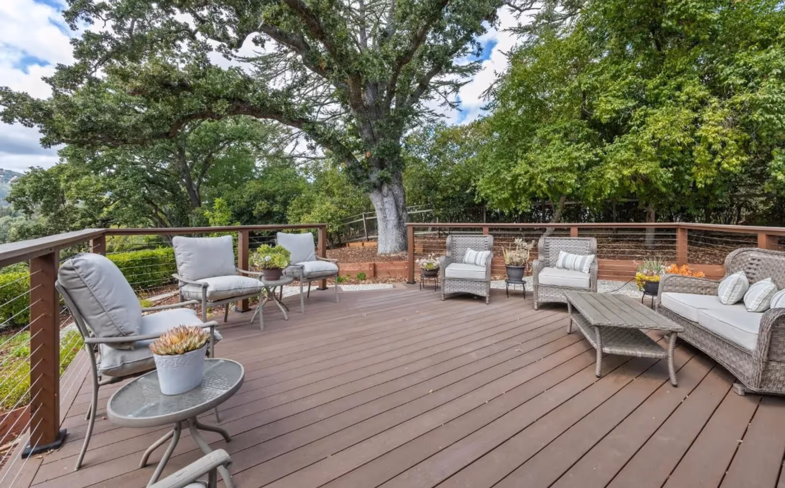 Expansive outdoor deck with wicker seating and surrounding green trees.