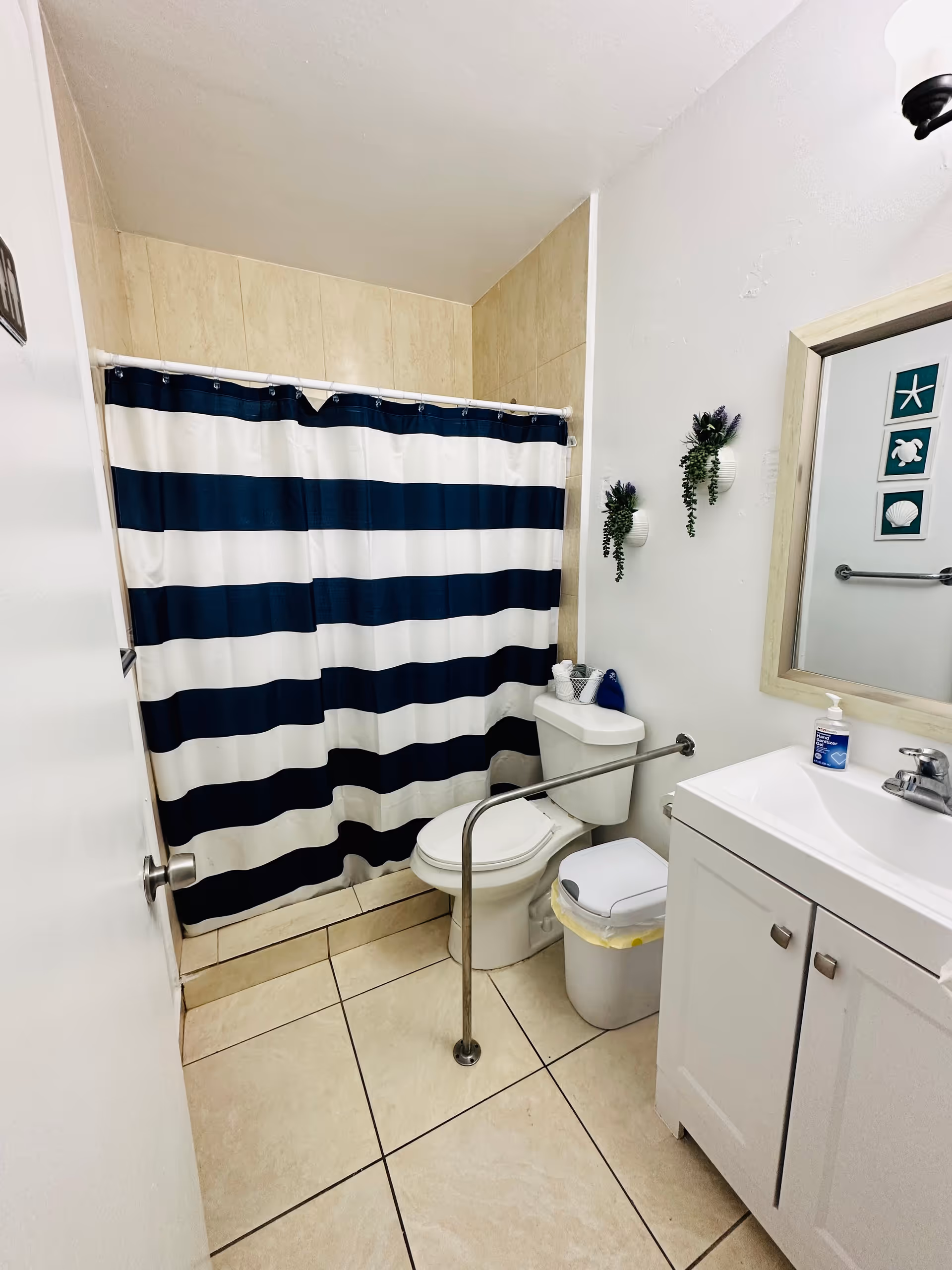 Small bathroom with striped navy shower curtain, toilet, sink, and grab bar.