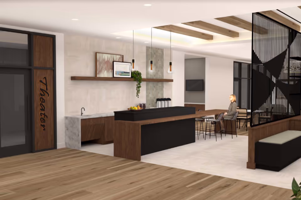 A modern communal interior with a central kitchen island, high seating, decorative partition, and a person seated at a table.