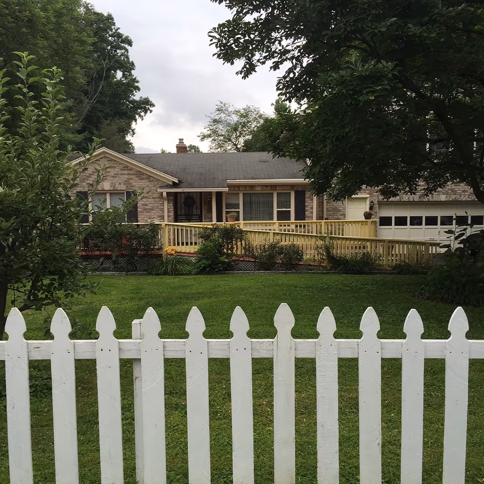 Front view of a single-story home with a white picket fence and greenery.