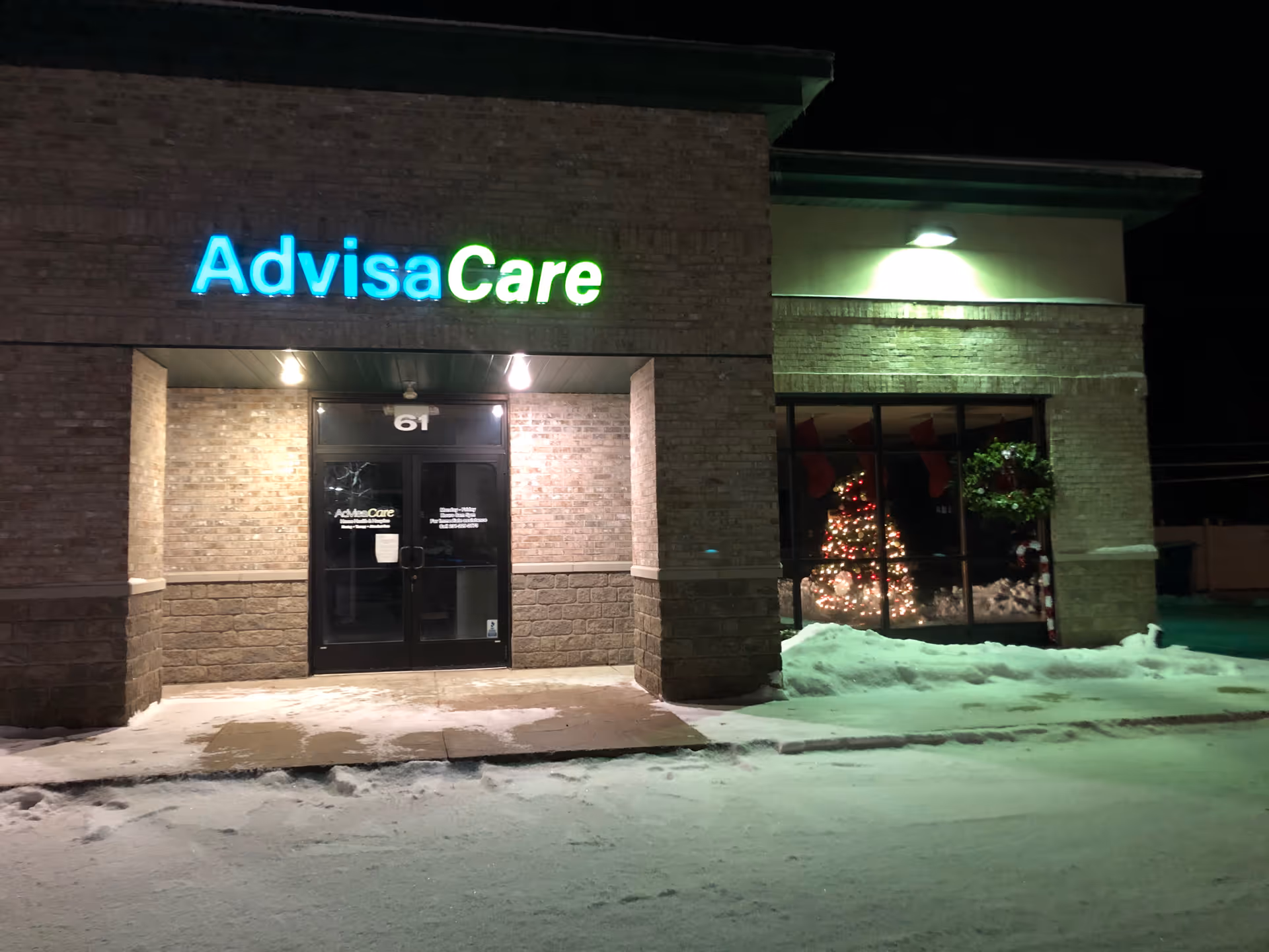 Night exterior of AdvisaCare building with illuminated sign and snowy ground.