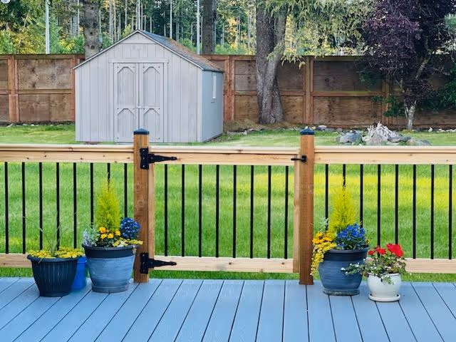 Blue deck with potted plants by a wooden railing and gray shed.