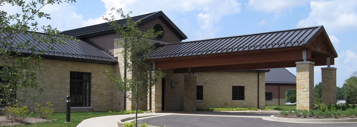 Stone hospice building with a covered entrance, driveway, and landscaped surroundings.