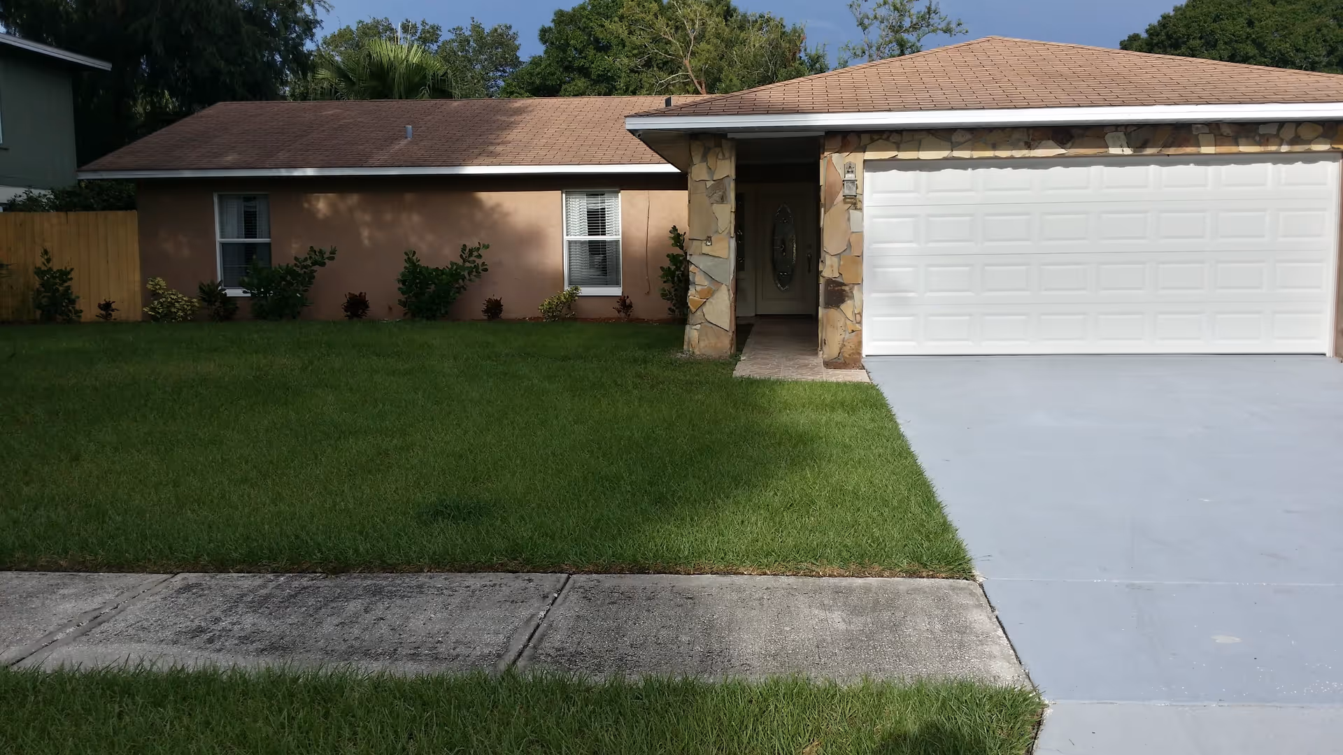 Single-story home's front exterior showing a white two-car garage, entryway with stone columns, and a green front lawn.