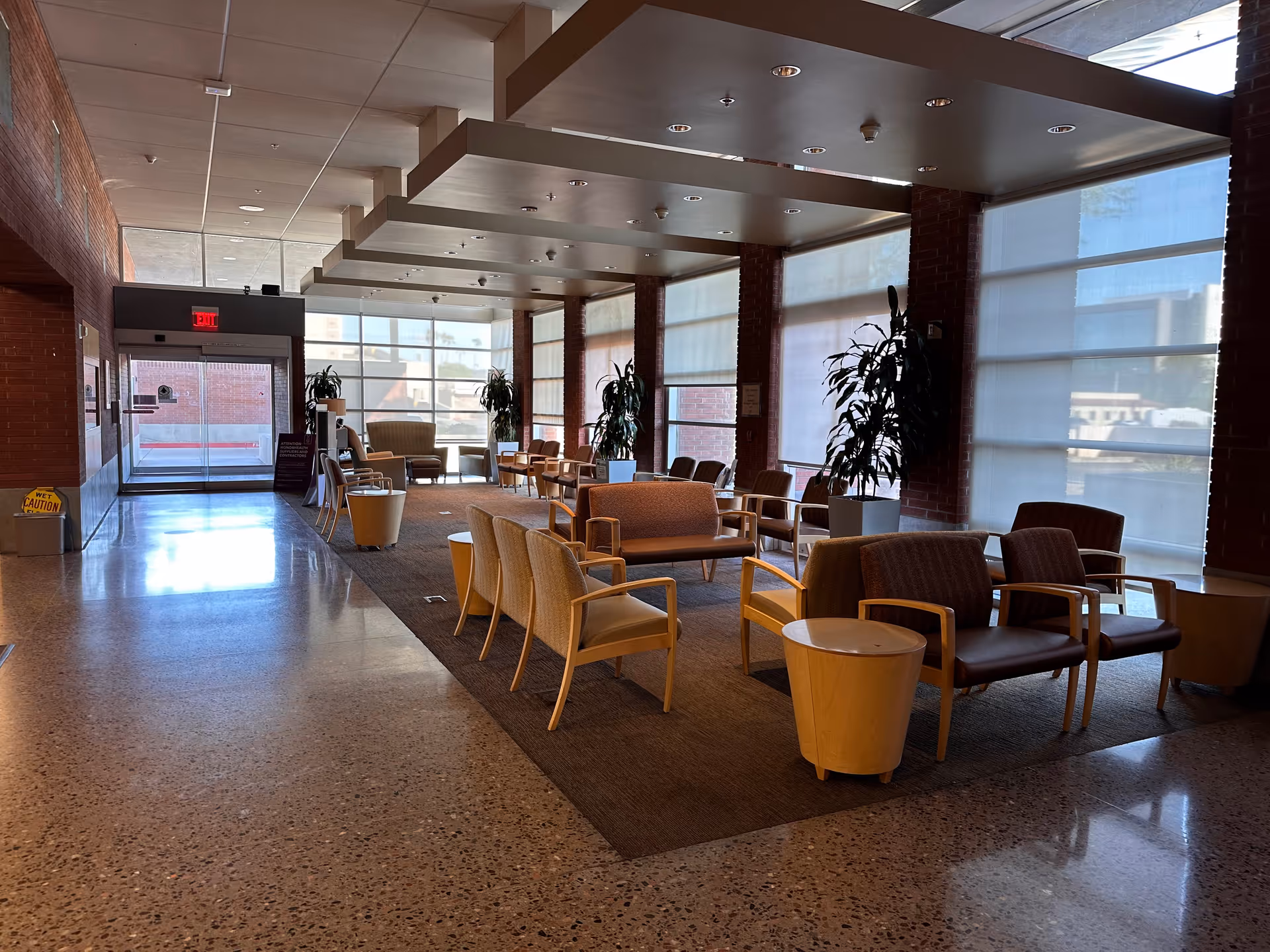 Interior hospital lobby with seating area, tables, plants, and large windows.