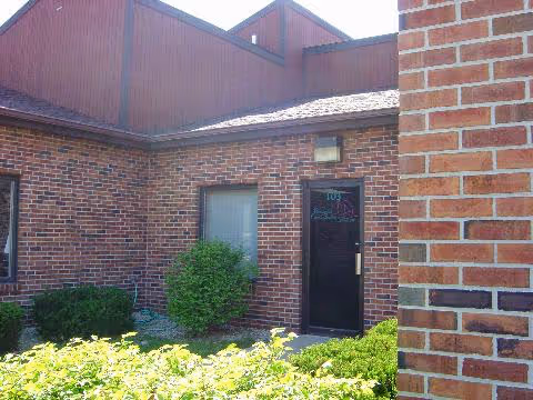 Brick exterior of a facility entrance with shrubs and a small window.