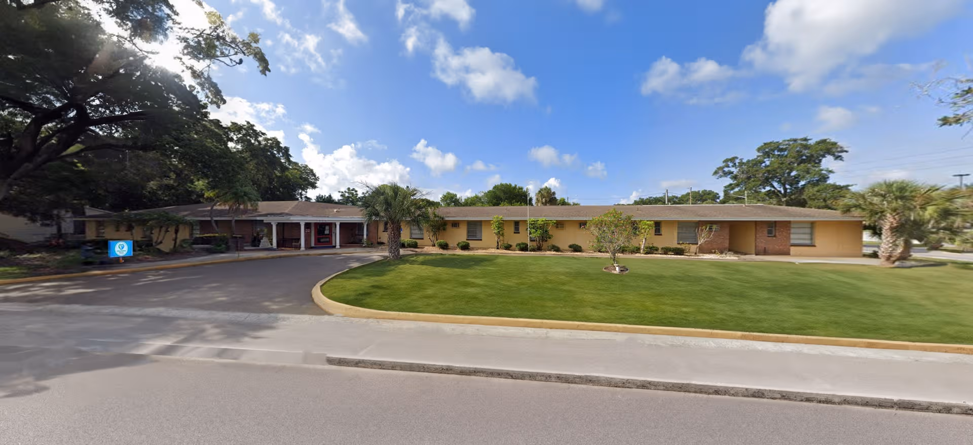Single-story beige senior living center with curved driveway and manicured front lawn.