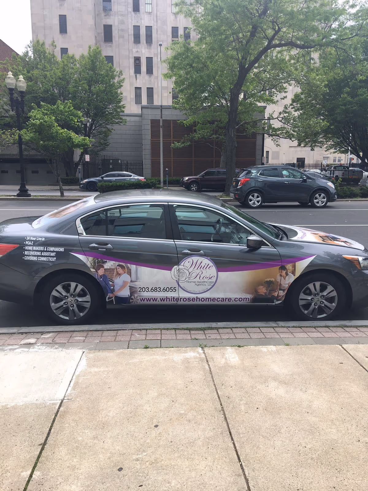 A sedan wrapped with White Rose Home Healthcare Agency ad parked on a city street.
