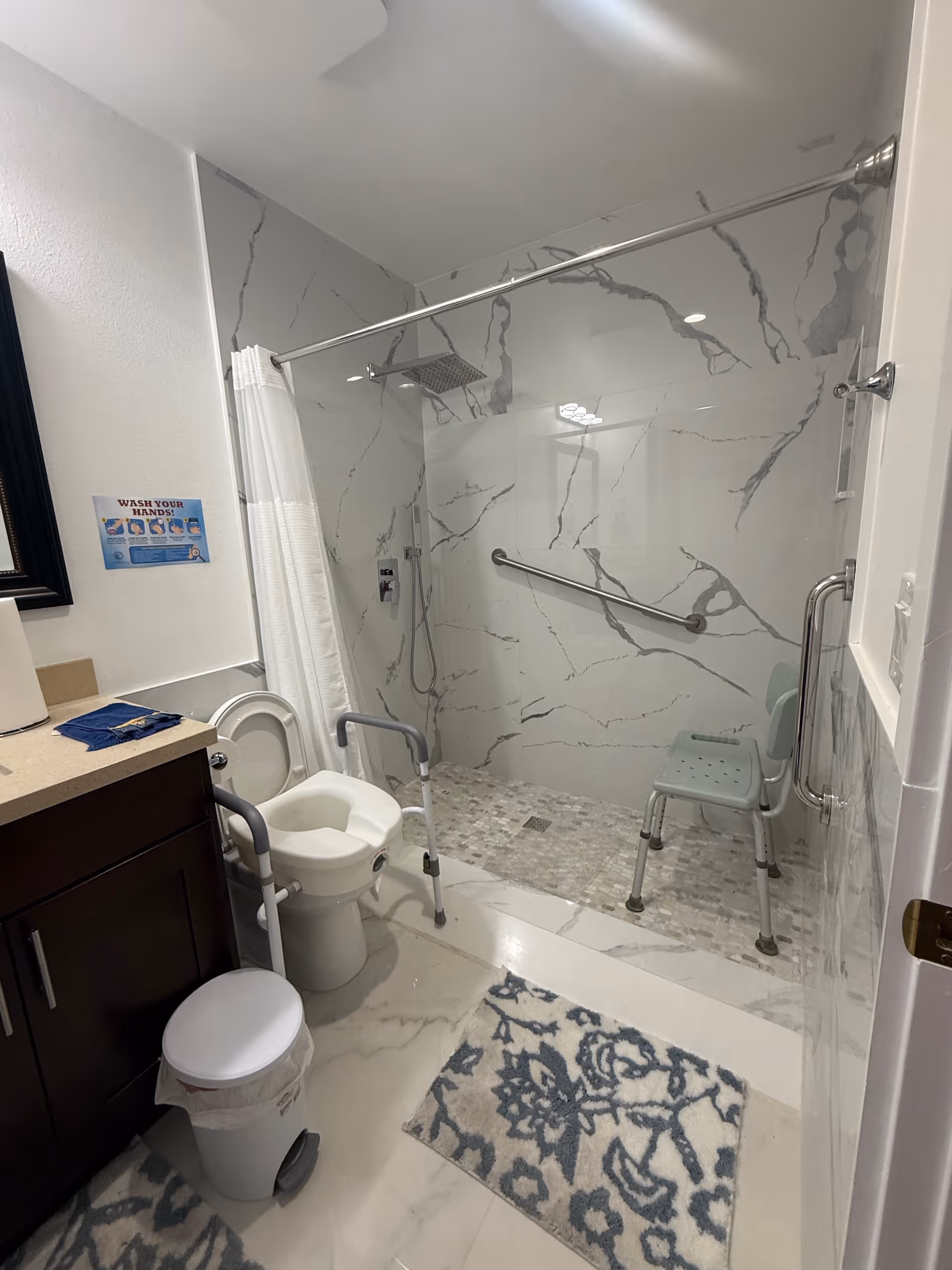 Accessible bathroom with marble shower walls, a chair, grab bars, and a toilet.