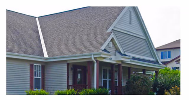 Exterior view of a senior living facility with a gray siding building and front porch.
