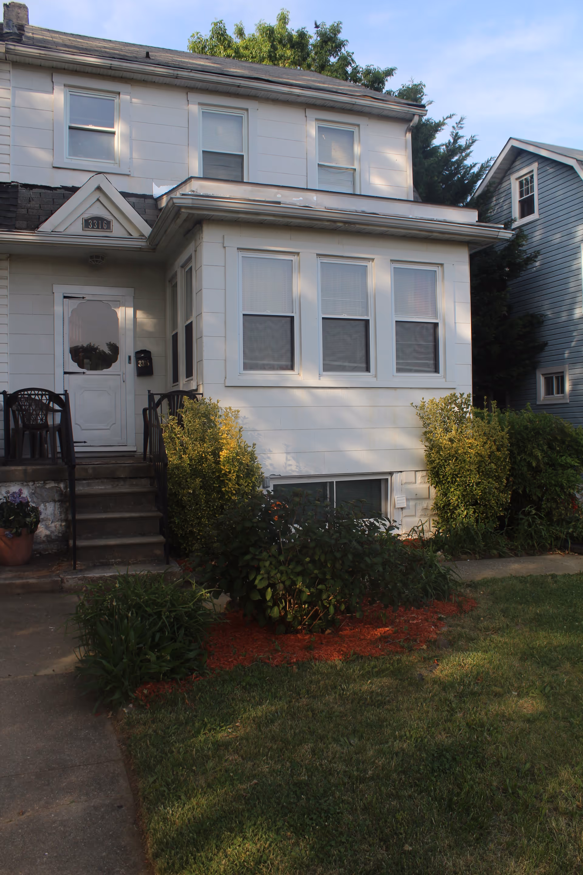 White two-story assisted living home with front steps, windows, and surrounding shrubs.