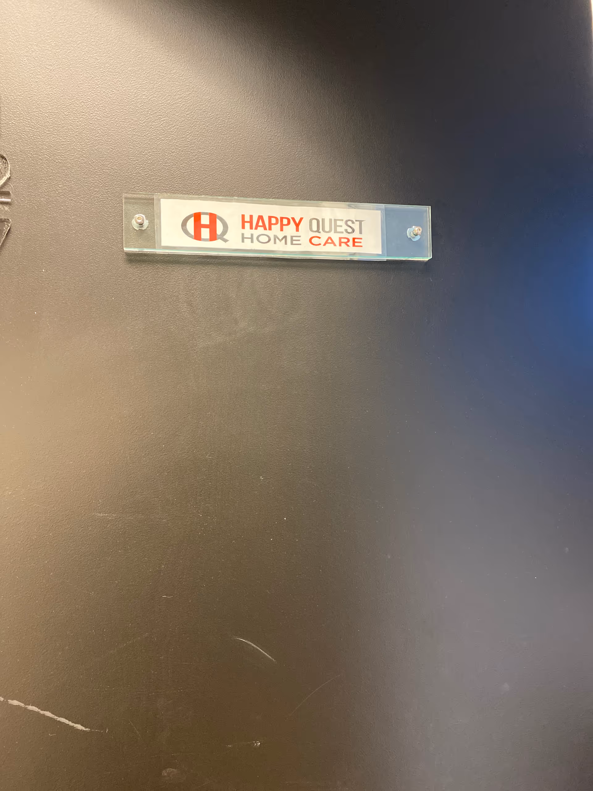 Clear plaque on a dark wall displaying Happy Quest Home Care logo.