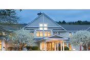 Front exterior of Harvest Hill senior living facility with glass doors and blooming trees
