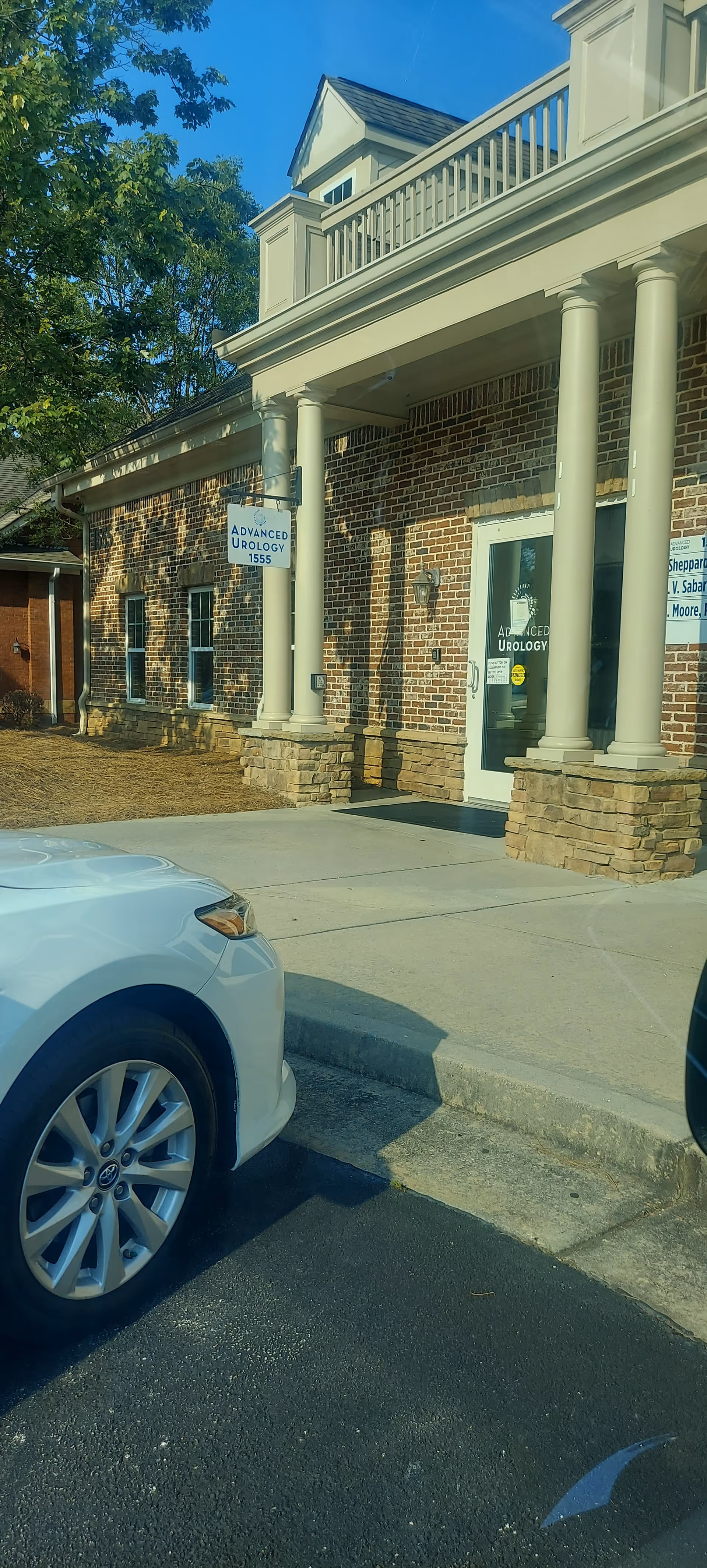 Brick building with columns and an entrance sign reading Advanced Urology, with a car in foreground.