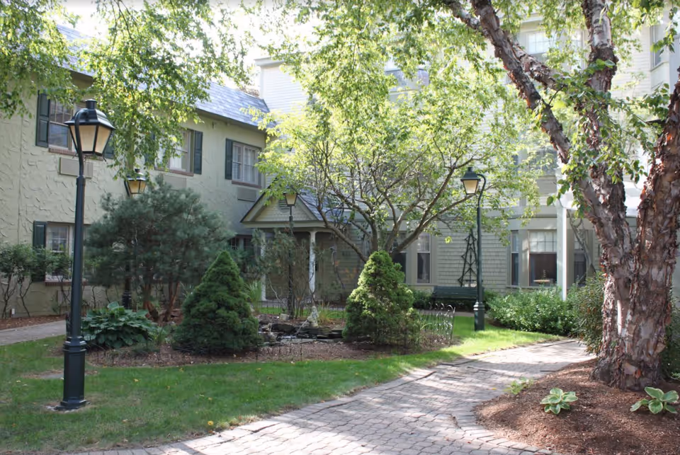 This exterior courtyard at Blaire House of Tewksbury features trees, shrubs, and lamp posts.