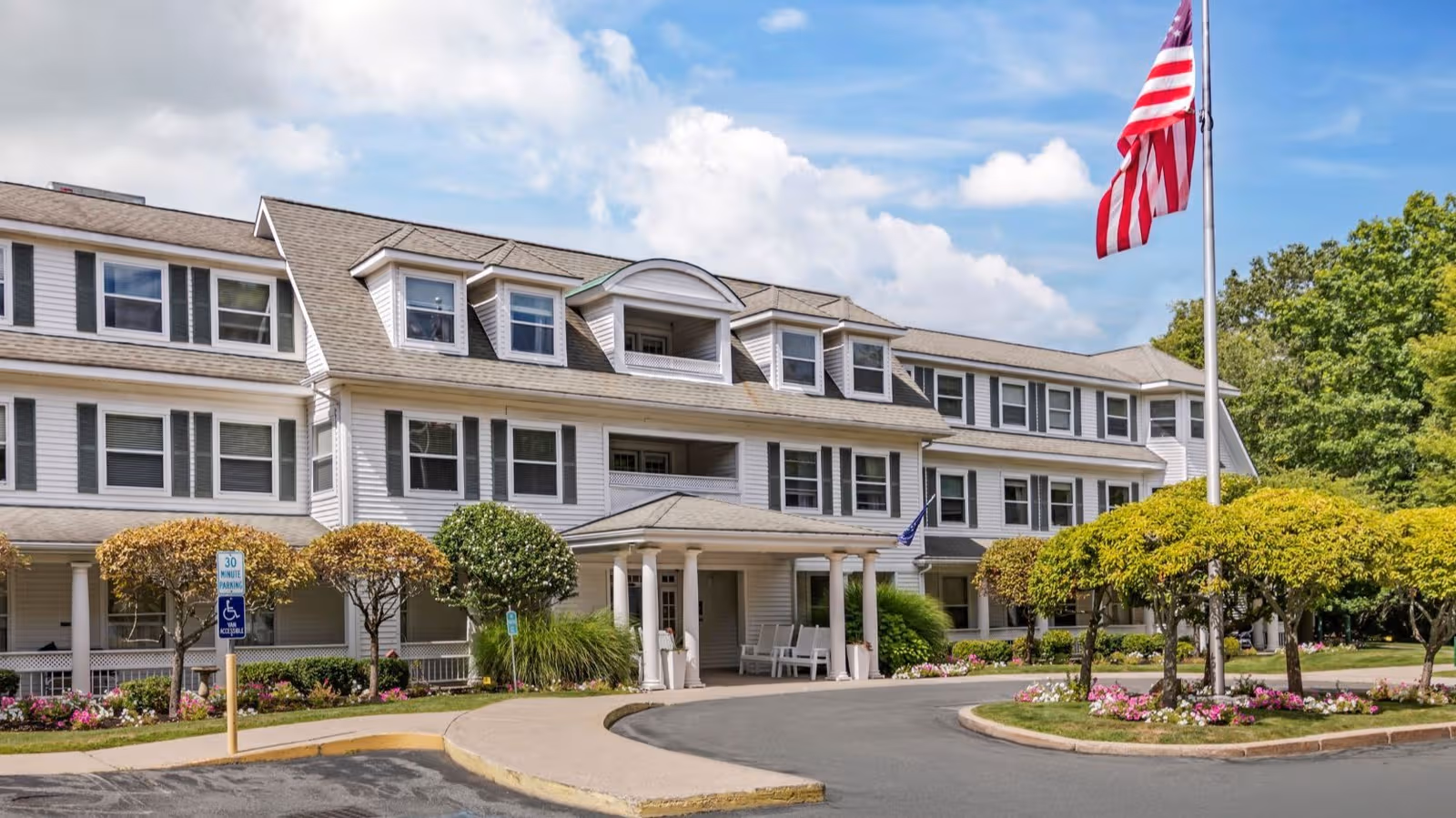 Exterior view of a multi-story senior living facility with a curved driveway and American flag.
