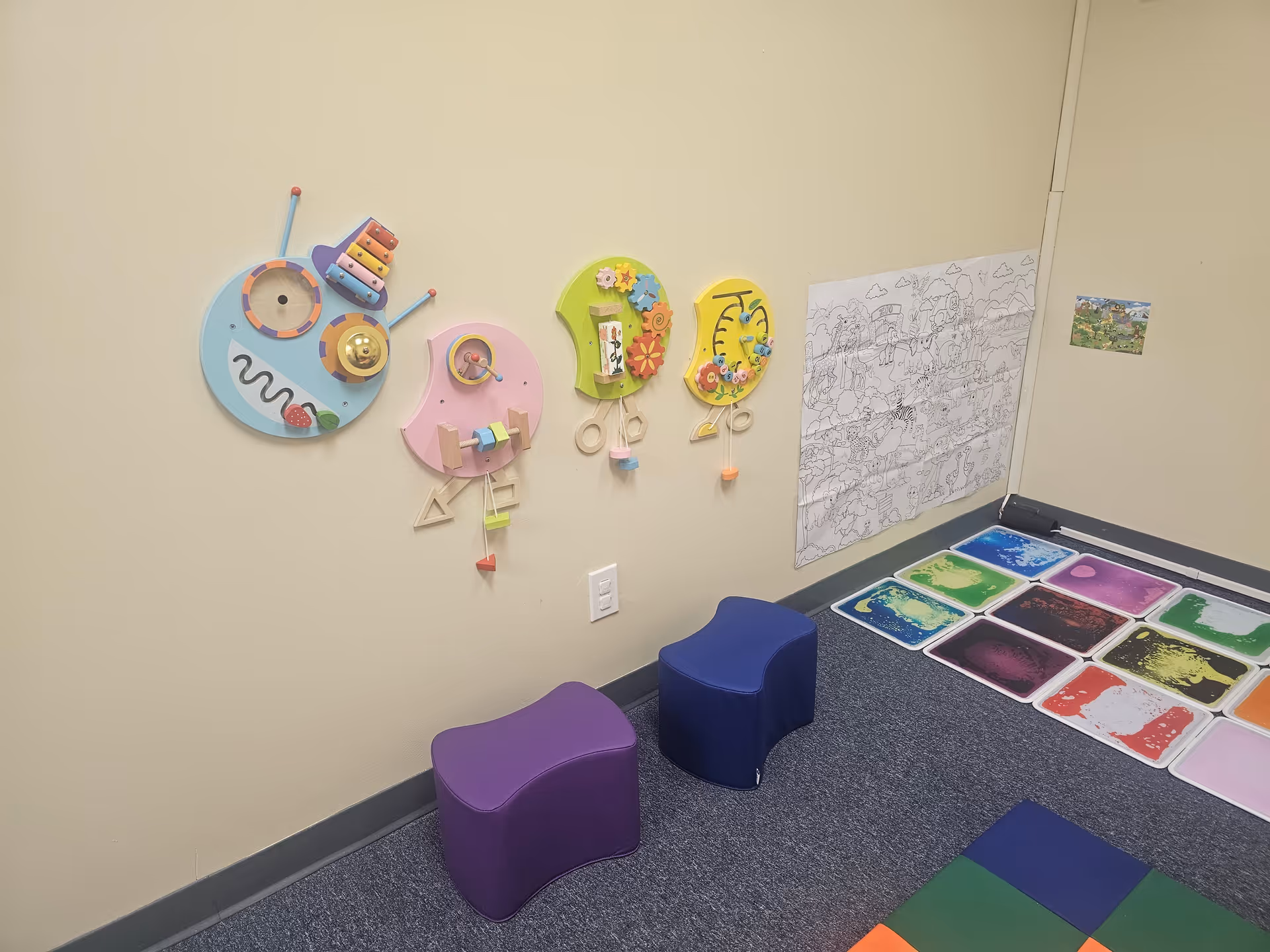 Colorful wall-mounted toys and bright floor mats in a small activity corner.