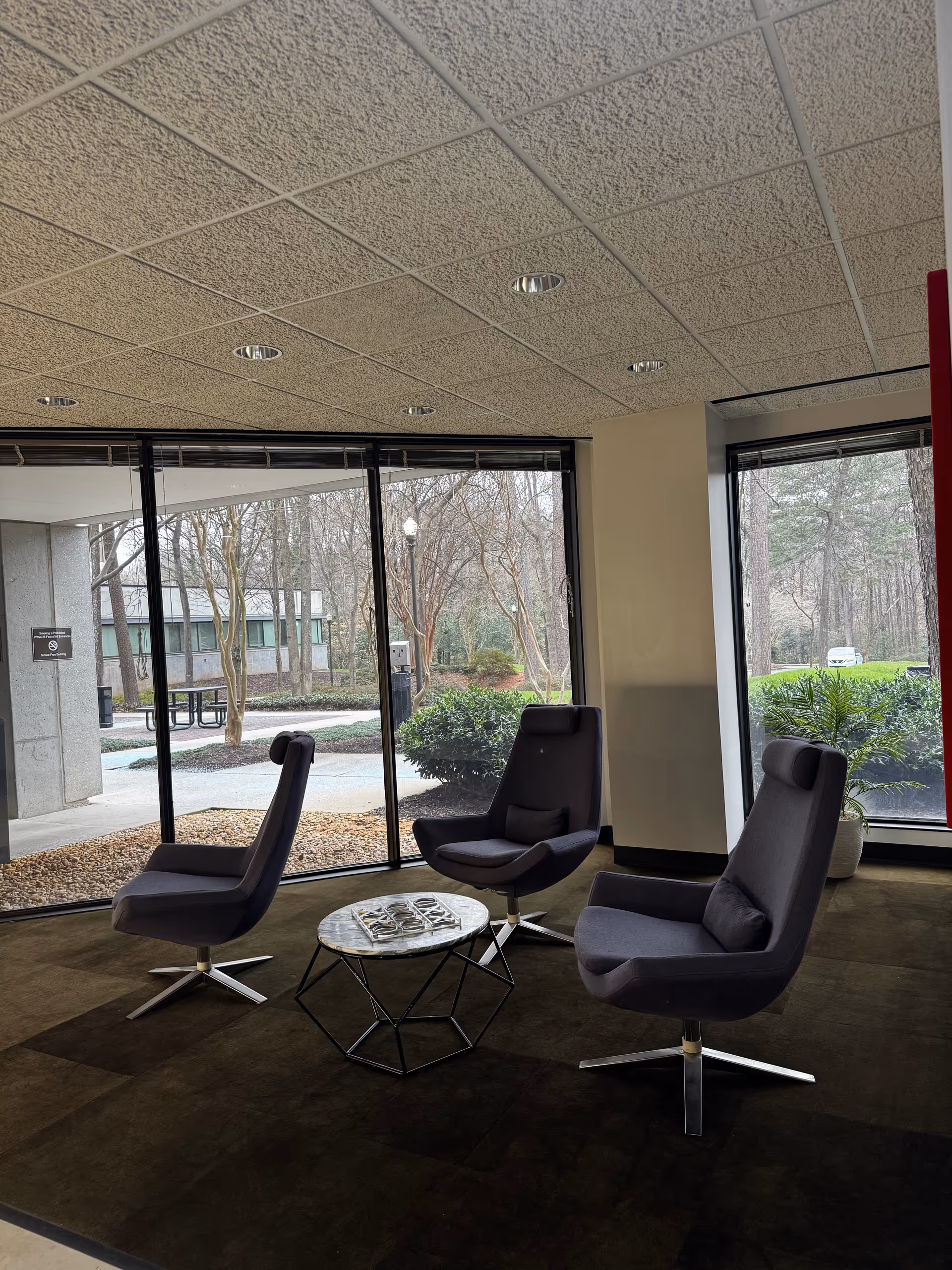 A modern indoor senior living facility lounge with three chairs around a small round table.