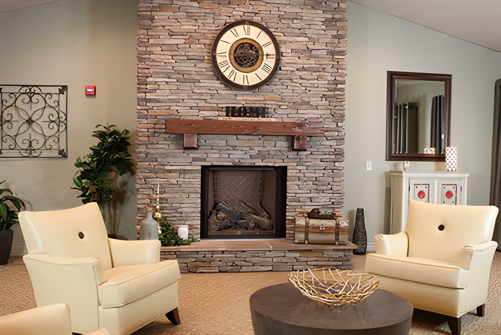 Cozy seating area with a stone fireplace, wall clock, two beige armchairs and a round coffee table.