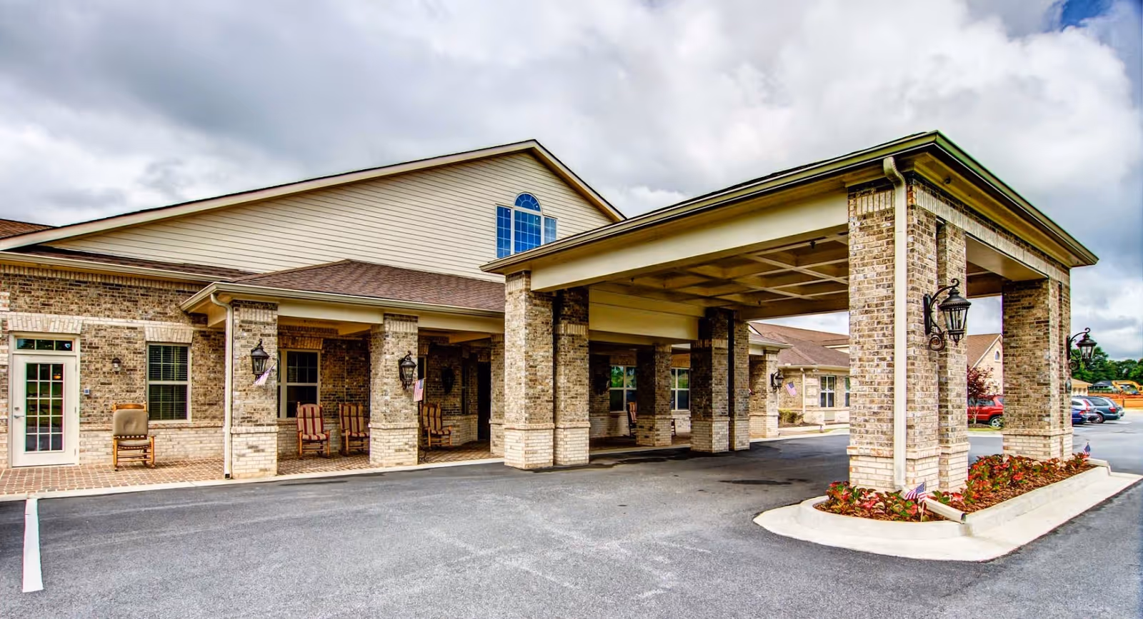 Brick senior living facility entrance with a covered drive-through and seating outside.