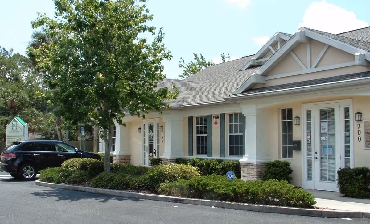 Exterior view of a beige senior living facility with entry doors and manicured landscaping.