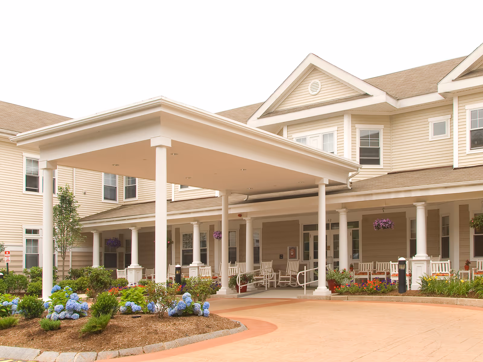 Exterior of a senior living facility with a covered entrance, white columns, and landscaped grounds