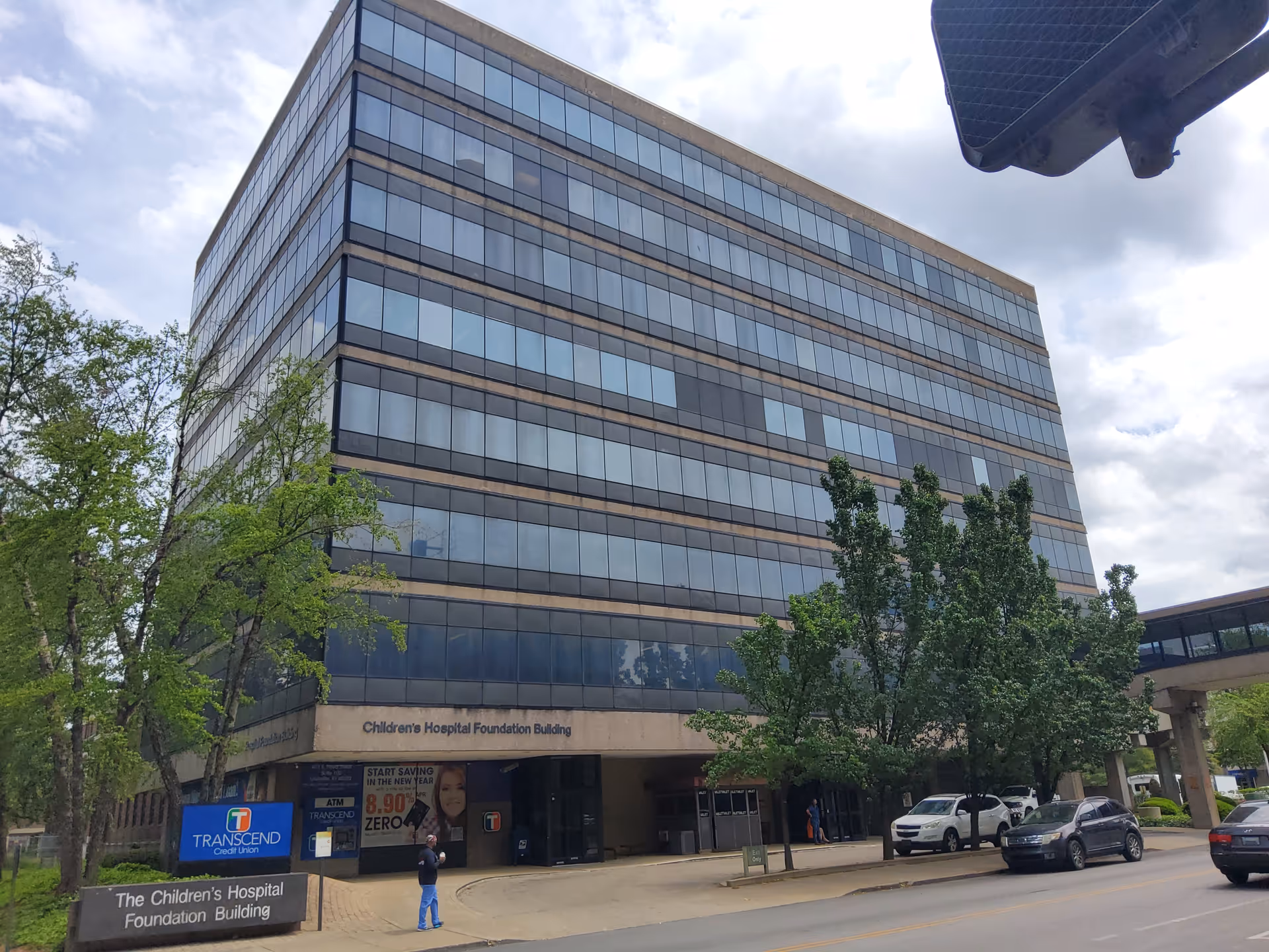 Tall glass-front building labeled Children's Hospital Foundation Building along a tree-lined street.