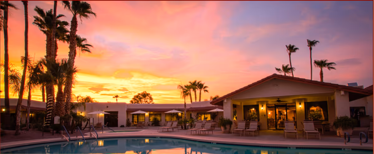 Sunset over a courtyard pool at Touch of Class Assisted Living, with lounge chairs.