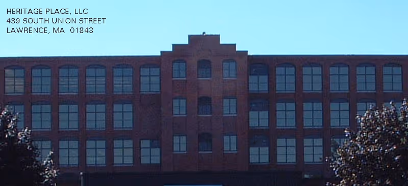 Brick multi-story building facade with many windows, viewed from street, featuring corner address text.