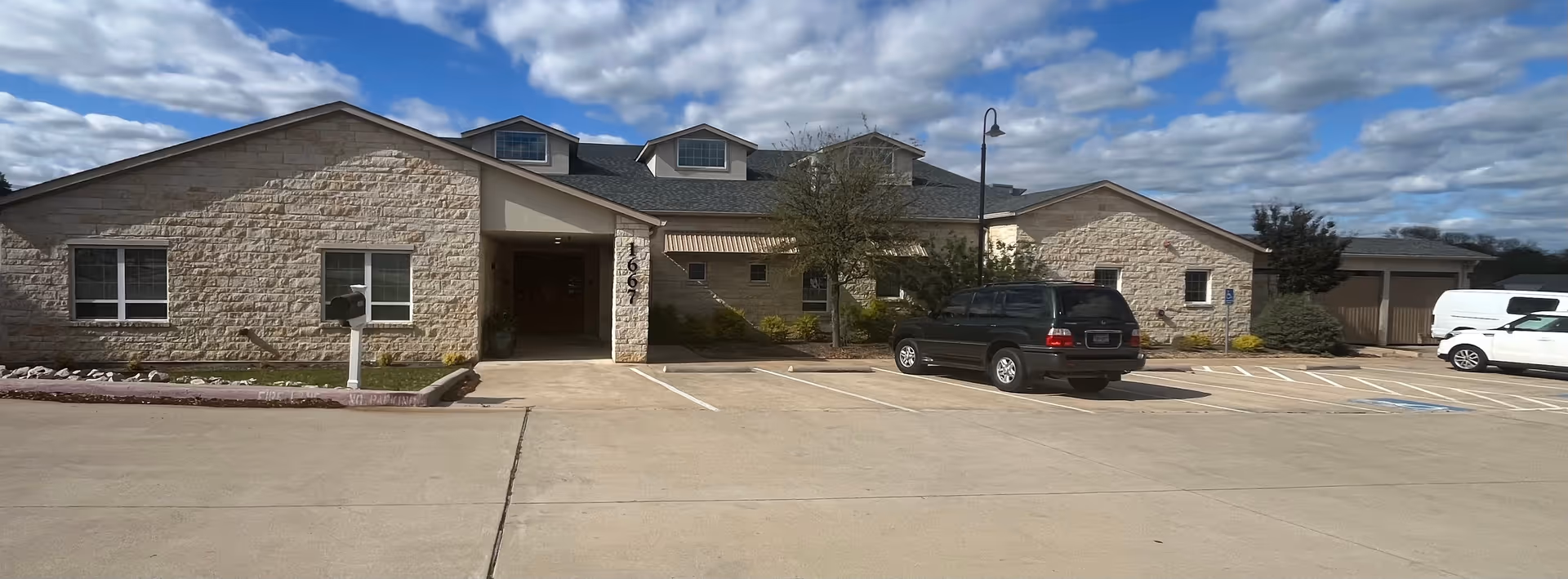 Front view of a single-story stone memory care building with parking.
