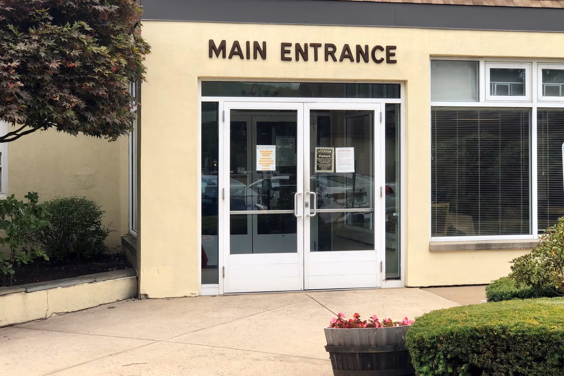Exterior view of Countryside Manor of Bristol main entrance with glass doors and landscaping.